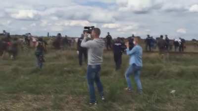 Hungarian journalist Petra Laszlo (blue shirt) trips a fleeing syrian refugee holding a child in an effort to get a good shot, causing him to be arrested by police. She was also taped kicking at other refugees
