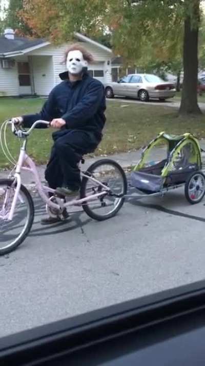 Michael Myers riding a pink bike as his wife scolds him.