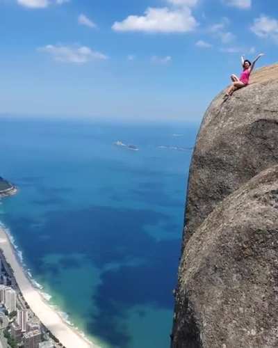 A tourist sitting on top of the Pedra da G&aacute;vea Mountain, Brazil