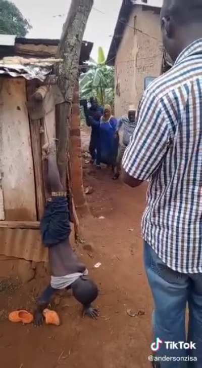 Uganda, East Africa. 10am in the rainy season. Woman administers this &ldquo;punishment&rdquo; to her orphaned stepson because he forgot to do dishes. He was there all night, got rescued in the morning after cries through the night.