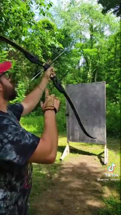 A guy shoots a bow through a ring while it was in the air