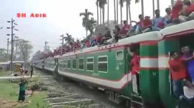 Train full of people passing under a bridge while another train full of people passes over the bridge.