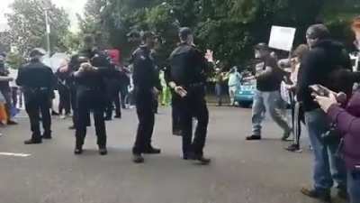 Policeman in Oregon flashing a white power sign at a Proud Boy
