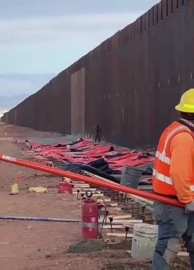 man climbs the us - mexico border while people are working on it