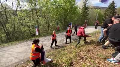 Drunk spectators wrestle in the middle of the road seconds before one of rally cars pass by at high speed