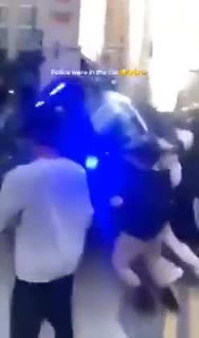 Rioters flipping over a police car with officers inside of it