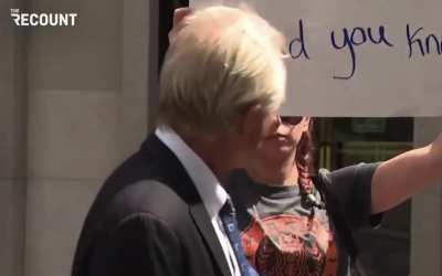 Former Trump advisor Peter Navarro attempts to to grab a determined protester's poster during a press conference