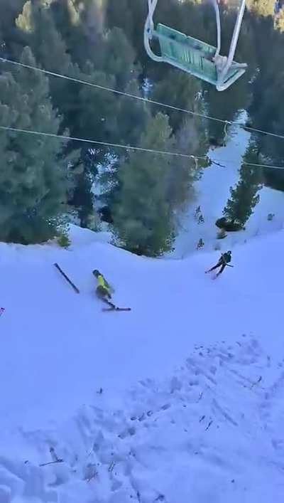 Two guys on a ski-lift filming a struggling snowboarder