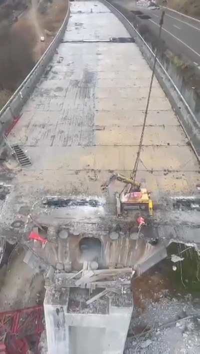 An airborne excavator demolishing a collapsed motorway bridge in Spain.
