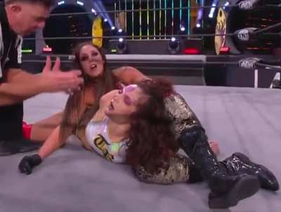 Britt Baker showing Thunder Rosa's unconscious face to the camera