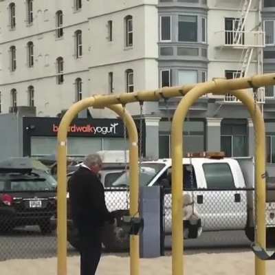 Just an old man pushing his dog on a swing