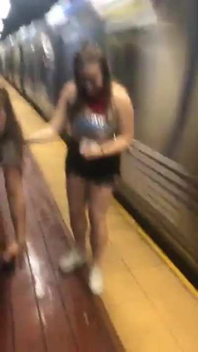Two drunk girls walking down subway platform as a subway train flies by...........