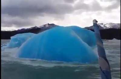 An aqua-blue iceberg emerging to the surface near a tourist boat off the coast of Argentina