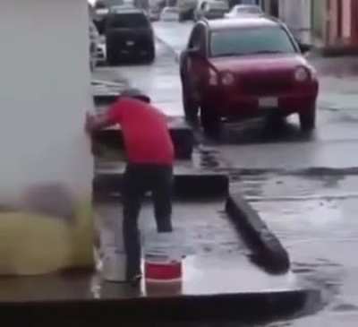 A guy walks across the flooded street with buckets on his feet to keep his shoes dry