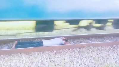 Guy lying on a railway track as a train passes over him