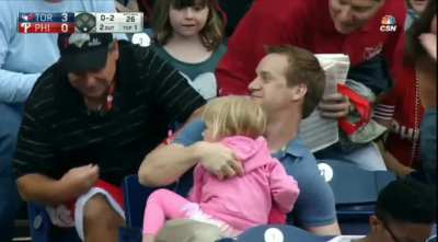 Man catches a baseball with one hand while his daughter's in his lap