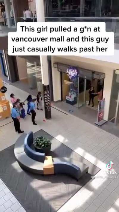 A guy with too little fucks to give walks past a woman who is threatening people with a gun