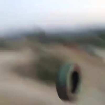 Man throws a tire down a hill at his friends.
