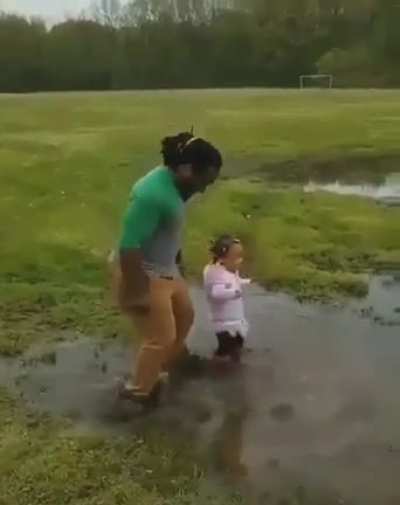 Dad jumps in puddle of water with his daughter. It&rsquo;s the little things that make kids happy.
