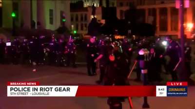 Studio tells journalists to keep getting closer to police line. Policeman uses them to sight in his paintball gun.