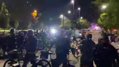 Man intentionally lays down in the road twice as Seattle police advance. First time they ride right by him, but the second time an officer walks his bike over the guy's hardhat.