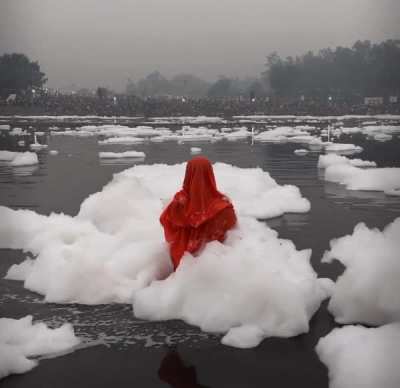 Woman praying in Yamuna river as toxic foam floats over her