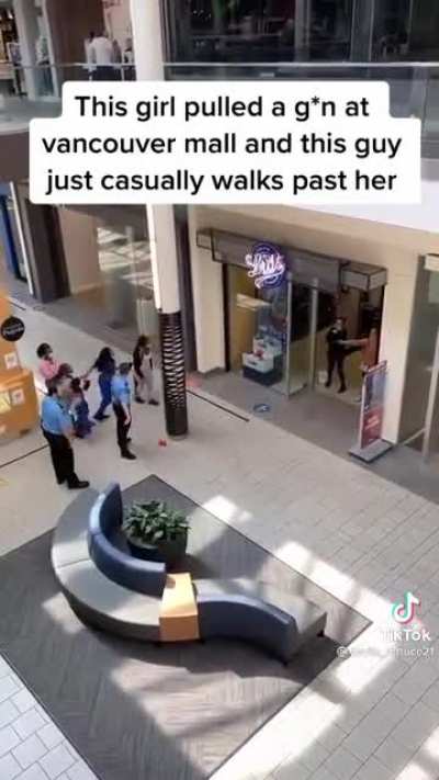 A guy with too little fucks to give walks past a woman who is threatening people with a gun