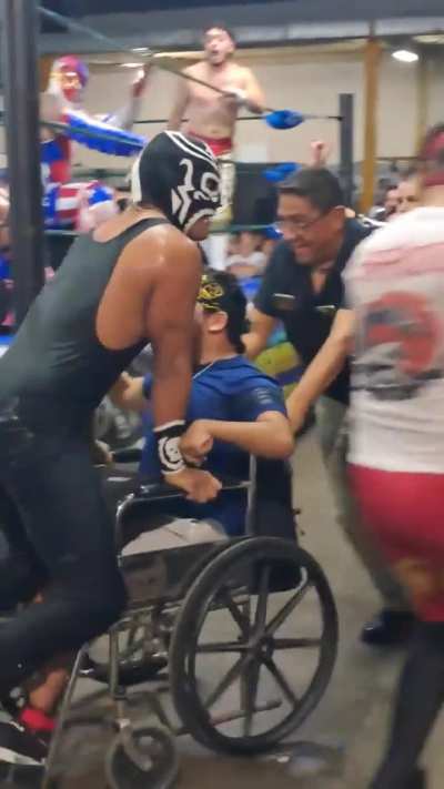 Mexican luchador Charro negro, being helped by a fan to avoid being eliminated touching the floor during a royal rumble match.