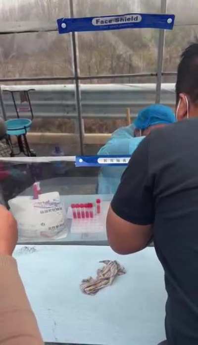 A nucleic acid test station worker casually smoking a cigarette, mask down, blowing smoke down people&rsquo;s throats and sneezing😅🤣