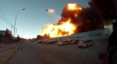 Burning warehouse explodes, sending a propane tank flying high.