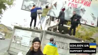 People tear the poster with the inscription "Kherson is Russian city" from the big board.