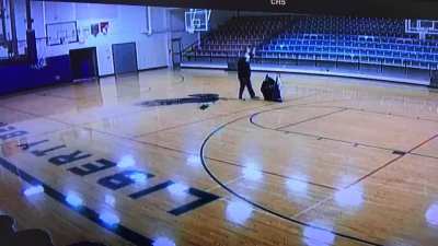 School custodian casually walking through the gym with no one watching but the security camera and making a cool shot look easy