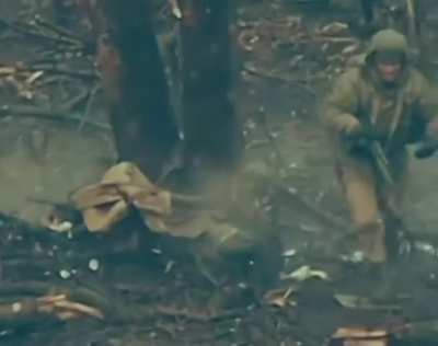 Two Russian soldiers drag an injured comrade. For an unknown reason they then leave him lying in the mud. The two soldiers then rest by a tree. A Ukrainian drone then hits the soldier on the left. The remaining Russian then covers his injured comrade and 