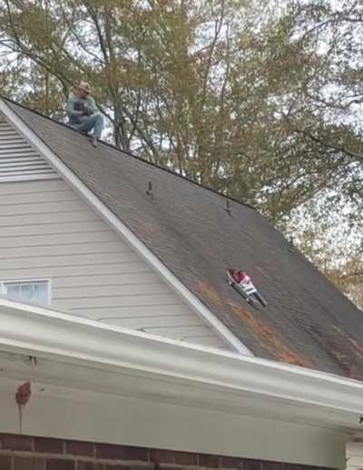 My neighbor using a blower taped to a skateboard on a rope to clean the roof