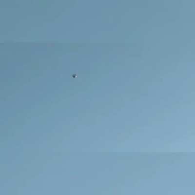 Stationary round metallic object with a helicopter circling it