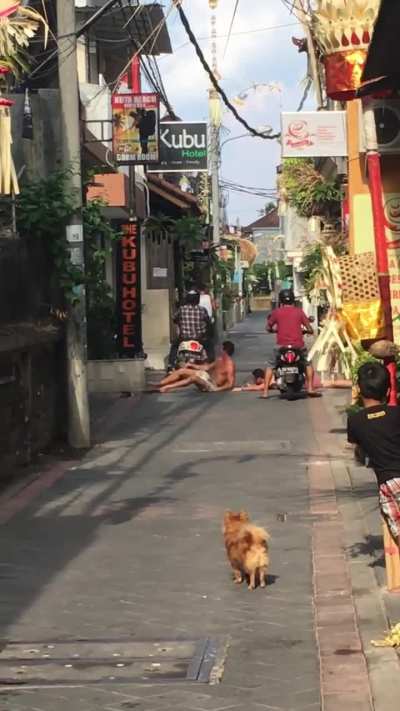 2 guys lie down on the ground and get run over by mopeds