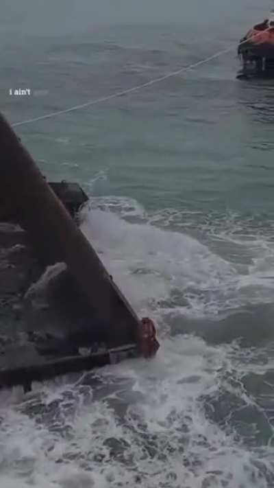 Man sits on a gigantic charcoal container that weighs slowly and heavily by the sea. It seems very dystopian and scary, just to be clear.